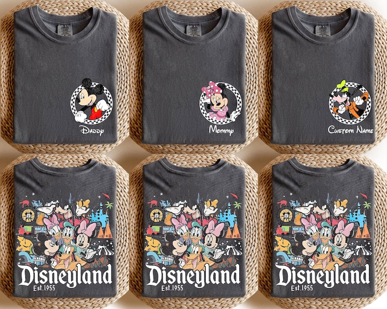 May include: Six dark grey t-shirts with Disney character designs. Three shirts feature Mickey, Minnie, and Goofy in circular frames with text. The other three shirts display a colourful Disneyland graphic with the text "Disneyland Est. 1955".
