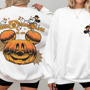 May include: White sweatshirt featuring a large orange pumpkin with Mickey Mouse ears and a smiling face. The back of the sweatshirt says "Walt Disney World" with Mickey Mouse and ghosts. The front has a small Mickey Mouse graphic.