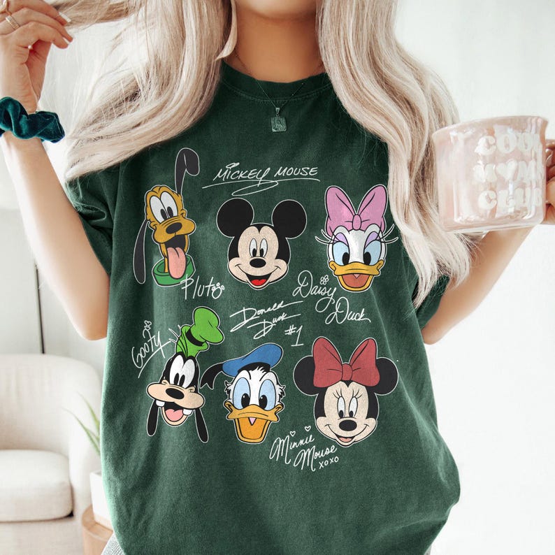 May include: A green t-shirt with a graphic print of Mickey Mouse, Minnie Mouse, Donald Duck, Daisy Duck, Goofy, and Pluto. The shirt has the text "Mickey Mouse", "Pluto", "Donald Duck #1", "Daisy Duck", "Goofy", and "Minnie Mouse XOXO" written on it.