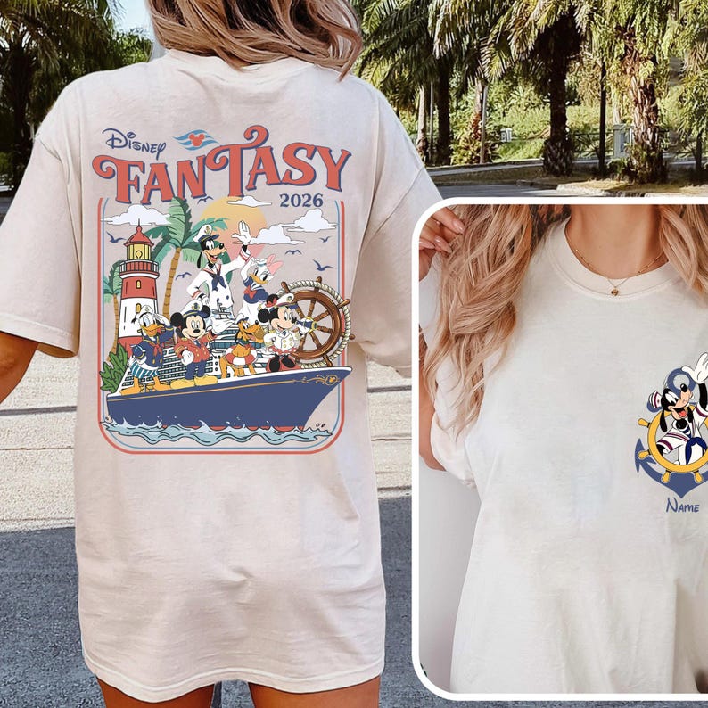 May include: Cream-colored t-shirt featuring a Disney Fantasy design. The back graphic showcases Disney characters on a ship with a lighthouse and the text "FANTASY 2026." A smaller graphic on the front includes Mickey Mouse and an anchor.
