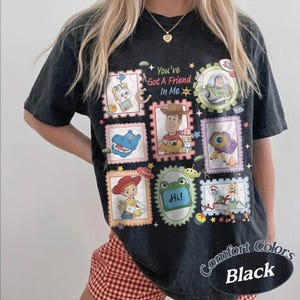 May include: A black short-sleeve t-shirt featuring a graphic print of various characters and objects from Toy Story arranged in postage stamp frames. The text "You've Got A Friend In Me" is printed in the center. The shirt has a vintage wash.