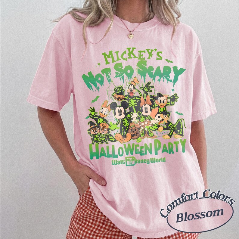 K&ouml;nnte beinhalten: Hellrosa T-Shirt mit einem gr&uuml;nen Aufdruck von Disney-Figuren in Halloween-Kost&uuml;men. Der Text lautet "Mickey's Not So Scary Halloween Party" und "Walt Disney World". Das Shirt ist ein Comfort Colors Blossom.