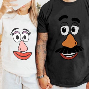 May include: Two short-sleeved t-shirts, one white and one black, each with a cartoon face design. The white shirt has a pink nose and red lips. The black shirt has a brown nose and a black moustache.