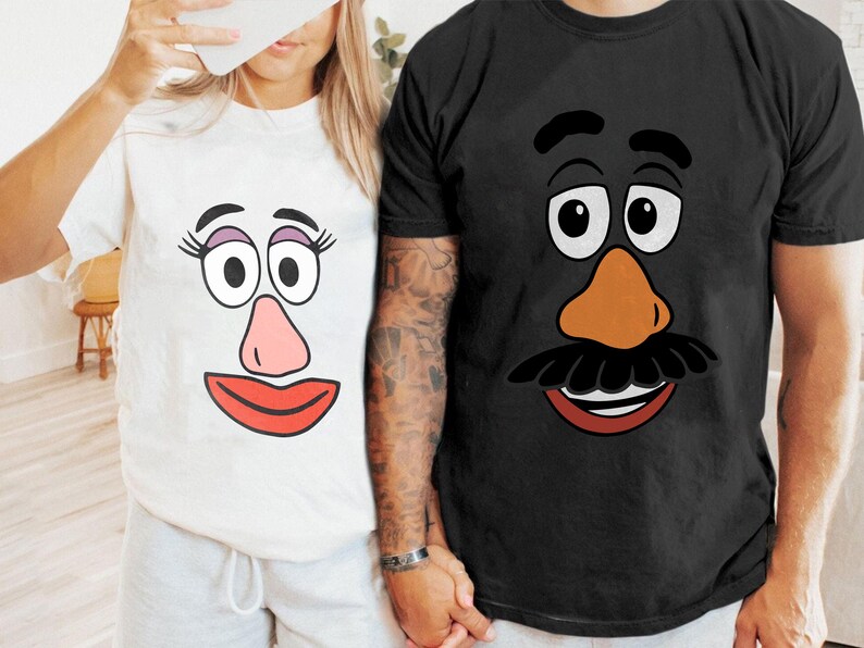 May include: Two short-sleeved t-shirts, one white and one black, each with a cartoon face design. The white shirt has a pink nose and red lips. The black shirt has a brown nose and a black moustache.