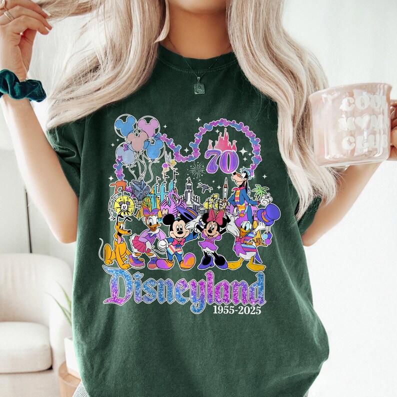 May include: Dark green t-shirt featuring a colorful Disneyland graphic. The design includes various Disney characters, balloons, a castle, and the text "Disneyland 1955-2025" celebrating its 70th anniversary. The shirt is a comfortable, casual style.