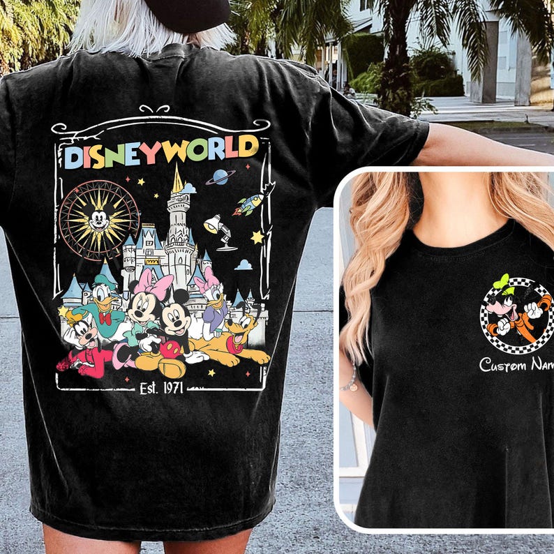 Op de afbeelding: Zwart T-shirt met een kleurrijke Disney World-afbeelding op de rug, met Mickey Mouse, Minnie Mouse en vrienden. De voorkant heeft een klein Goofy-ontwerp. De tekst "Est. 1971" is ook zichtbaar.