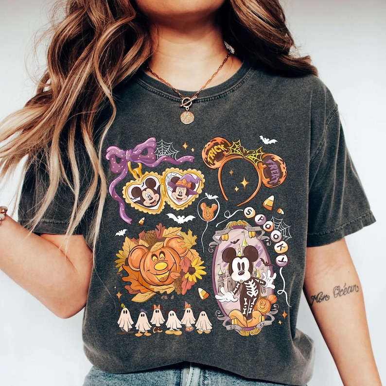 May include: Dark gray t-shirt featuring a colorful Halloween-themed graphic. The design includes Mickey Mouse in a skeleton costume, a pumpkin, ghosts, and the words "Trick or Treat" on a headband. The shirt has a vintage wash.