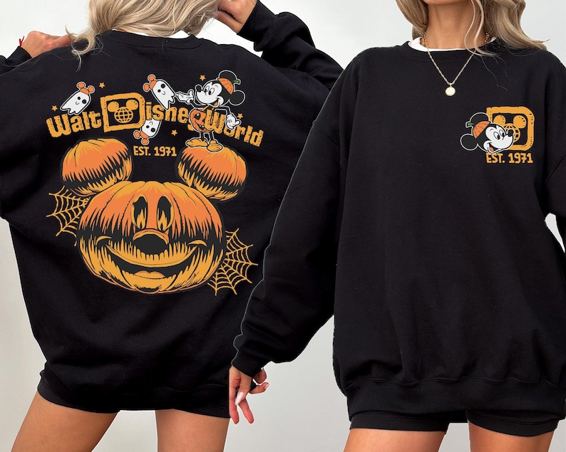 May include: Black sweatshirt featuring a Halloween-themed Walt Disney World design. The design includes a smiling jack-o'-lantern, Mickey Mouse, ghosts, and the text "Walt Disney World EST. 1971". The sweatshirt has a white collar.