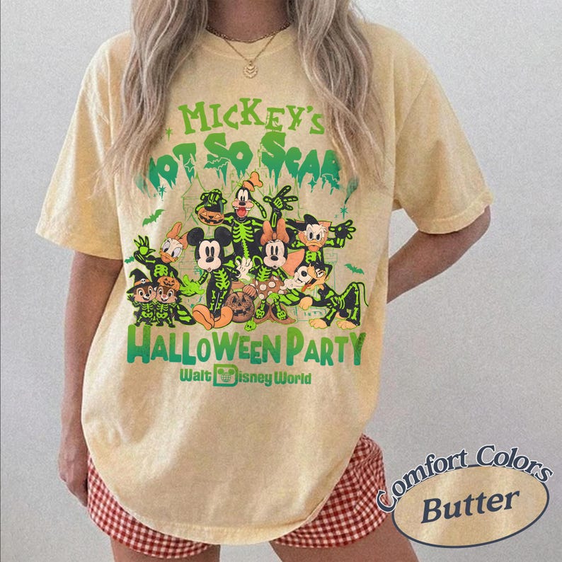 K&ouml;nnte beinhalten: Ein hellgelbes T-Shirt mit einem Halloween-Motiv mit Disney-Figuren in Skelett-Kost&uuml;men. Der Text lautet "Mickey's Not So Scaaary Halloween Party" und "Walt Disney World". Das Shirt ist mit "Comfort Colors Butter" gekennzeichnet.