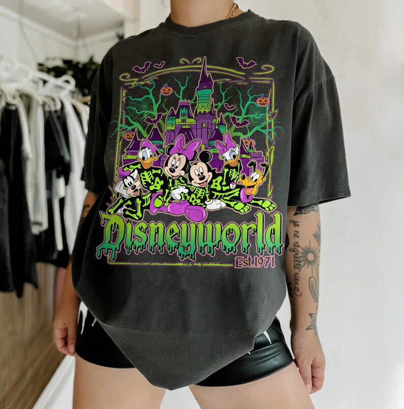 May include: Dark gray t-shirt featuring a Halloween-themed Disney World graphic. The design includes cartoon characters in skeleton costumes, a spooky castle, bats, and pumpkins. The text "Disneyworld Est. 1971" is also visible.