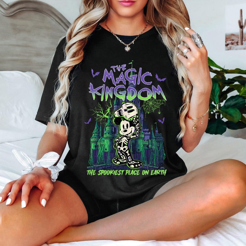 May include: Black t-shirt with a spooky Mickey Mouse design. The graphic shows Mickey as a skeleton holding a skull, in front of a green and purple castle. Text reads "The Magic Kingdom" and "The Spookiest Place on Earth."