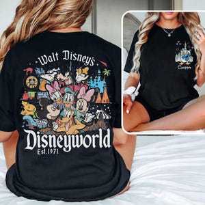 May include: Black t-shirt featuring a colorful Disney World graphic on the back with Mickey, Minnie, Donald, and Goofy. The front of the shirt has a smaller graphic of a castle and Donald Duck with the word "Custom".