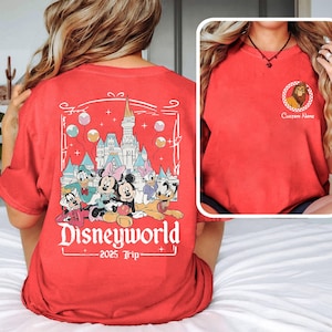 May include: Red t-shirt with a graphic of Mickey Mouse and friends in front of Cinderella's Castle at Disney World. The text "Disneyworld 2025 Trip" is printed below the graphic.