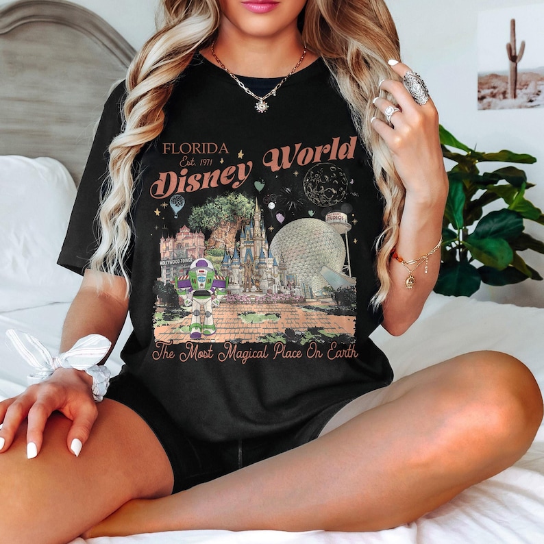 May include: Black t-shirt featuring a colorful graphic of Disney World in Florida. The design includes the text "Florida Disney World Est. 1971" and "The Most Magical Place On Earth". The graphic showcases iconic park elements like Cinderella's castle and Spaceship Earth.