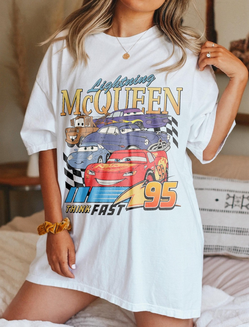 May include: White oversized t-shirt with a graphic print of Lightning McQueen and other Cars characters. The graphic includes the text "Lightning McQueen", "Think Fast", and "95".