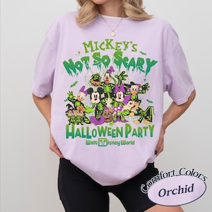 Op de afbeelding: Een lichtpaars T-shirt met een Halloween-thema Disney-afbeelding. Het ontwerp bevat verschillende personages in kostuums, met de tekst "Mickey's Not So Scary Halloween Party" in het groen. Comfort Colors merk, kleur Orchid.
