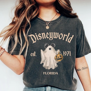 Op de afbeelding: Een zwart T-shirt met een vintage-stijl afbeelding van een geest die een jack-o'-lantern vasthoudt. De tekst "Disneyworld est. 1971 Florida" is op het shirt gedrukt.