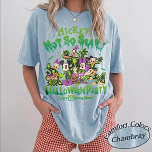 Op de afbeelding: Lichtblauw T-shirt met een Halloween-afbeelding met Mickey Mouse en vrienden in skeletkostuums. De tekst luidt "Mickey's Not So Scary Halloween Party" en "Walt Disney World". Het shirt is een Comfort Colors Chambray.