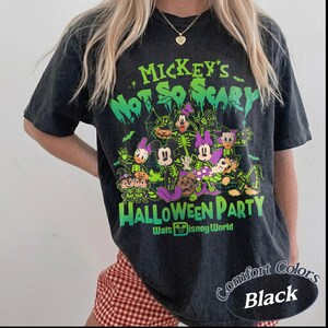 Op de afbeelding: Zwart Comfort Colors T-shirt met een Halloween-afbeelding. Het ontwerp toont Disney-personages en de tekst "Mickey's Not So Scary Halloween Party".