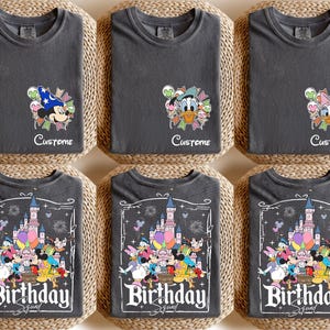 May include: Six charcoal gray t-shirts with different Disney character designs. The top row features Mickey Mouse, Donald Duck, and Daisy Duck with the word "Custome" below. The bottom row has a "Birthday Squad" design with Disney characters and a castle.