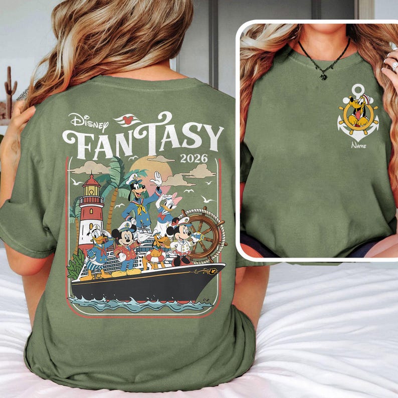 May include: Olive green t-shirt featuring a Disney Fantasy cruise ship design. The back of the shirt displays a colorful graphic of Disney characters on a ship, with the text "Disney Fantasy 2026". The front has an anchor design with Pluto.