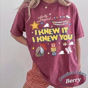 May include: A berry-coloured t-shirt featuring the text "infinity and beyond", "I KNEW IT I KNEW YOU", and "YOU'VE GOT A FRIEND IN ME". Graphics include a yellow star, a beaded bracelet, a cowboy boot, alphabet blocks with "TSS 5", and a bow.