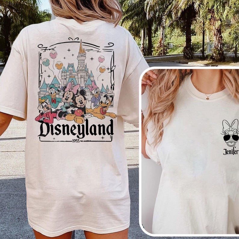 K&ouml;nnte beinhalten: Zwei wei&szlig;e T-Shirts. Die R&uuml;ckseite eines Shirts zeigt ein Motiv von Mickey Mouse und seinen Freunden vor dem Disneyland-Schloss mit dem Text "Disneyland - 1955". Die Vorderseite des anderen Shirts zeigt ein Schwarzwei&szlig;-Motiv von Minnie Mouse mit Sonnenbrille und dem Text "Jenifer".