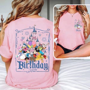 K&ouml;nnte beinhalten: Hellrosa T-Shirt mit einem Disney-Schloss und Figuren wie Mickey und Minnie Mouse, Donald Duck und Goofy. Auf der R&uuml;ckseite des Shirts steht in blauer Schrift "Birthday Squad". Ein kleineres Bild auf der Vorderseite zeigt "Sister".