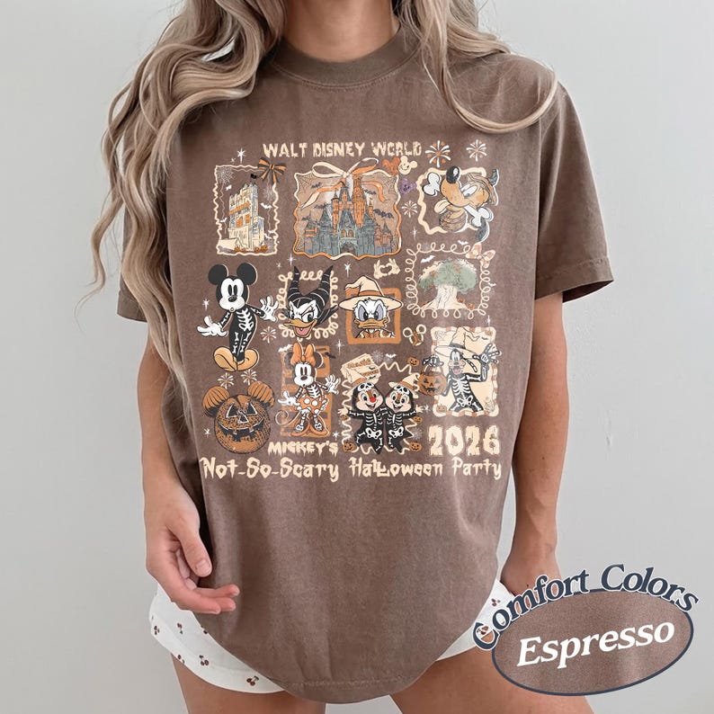Pu&ograve; includere: T-shirt color espresso con un design grafico di personaggi Disney in costume di Halloween. La maglietta include il testo "Walt Disney World", "Mickey's Not-So-Scary Halloween Party" e "2026". &Egrave; una maglietta del marchio Comfort Colors.