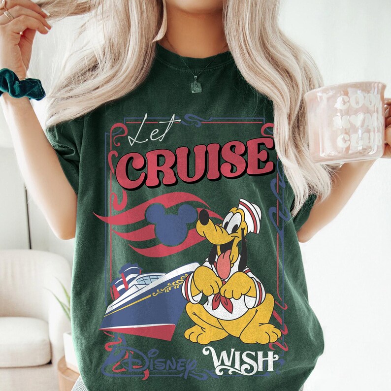Może przedstawiać: Ciemnozielona koszulka z grafiką z napisem "Let Cruise" w kolorze czerwonym i białym, postacią z kresk&oacute;wki Pluto i statkiem wycieczkowym. Koszulka zawiera r&oacute;wnież napis "Disney Wish".