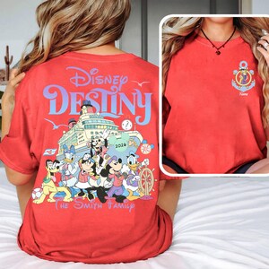 May include: Red t-shirt featuring the words "Disney Destiny" above a graphic of a cruise ship with Disney characters. The shirt also includes the text "The Smith Family" and a small anchor design with a character's image.