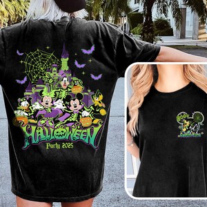 Op de afbeelding: Zwart T-shirt met een Halloween-ontwerp met Mickey Mouse, Donald Duck en Goofy. Het ontwerp bevat een spookkasteel, vleermuizen en de tekst "Halloween Party 2025". Een kleiner ontwerp staat op de voorkant.