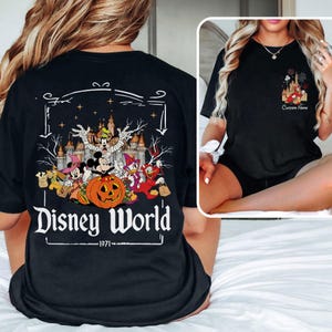 May include: Black t-shirt featuring a Halloween-themed Disney World graphic. The design includes Mickey Mouse as a mummy, a pumpkin, and other characters in costume. The text "Disney World - 1971" is printed below the graphic.