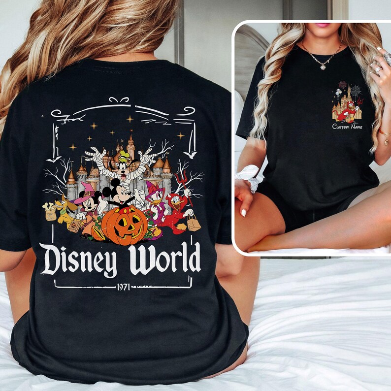 May include: Black t-shirt featuring a Halloween-themed Disney World graphic. The design includes Mickey Mouse as a mummy, a pumpkin, and other characters in costume. The text "Disney World - 1971" is printed below the graphic.