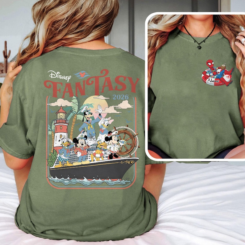 May include: An olive green t-shirt with a Disney Fantasy 2026 design on the back. The graphic shows Mickey Mouse, Minnie Mouse, Donald Duck, Goofy, and other characters on a cruise ship. A smaller graphic of Spider-Man and Santa Claus is on the front.