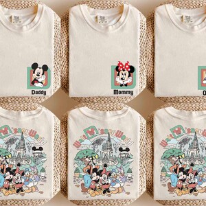 Puede incluir: Camisetas color crema con personajes de Disney y texto. Una camiseta tiene a Mickey Mouse con "Daddy", otra a Minnie Mouse con "Mommy", y una tercera a Daisy Duck con "Olivia". Las camisetas inferiores muestran un gr&aacute;fico colorido de Disney World.