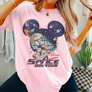 May include: Pink t-shirt with a graphic of Mickey Mouse and friends riding a space mountain ride. The graphic includes the text "Disney Space Mountain".