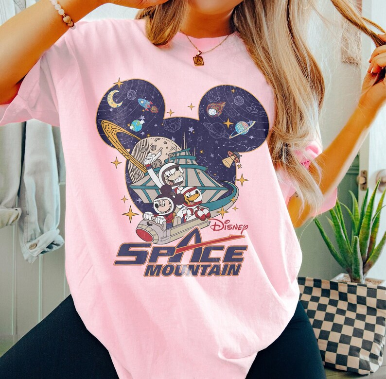 May include: Pink t-shirt with a graphic of Mickey Mouse and friends riding a space mountain ride. The graphic includes the text "Disney Space Mountain".