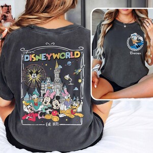 Op de afbeelding: Donkergrijs T-shirt met een Disney World-afbeelding op de achterkant, met Mickey Mouse, Minnie Mouse, Donald Duck, Daisy Duck en Pluto. De voorkant heeft een kleine Donald Duck-afbeelding en het woord "Brother".