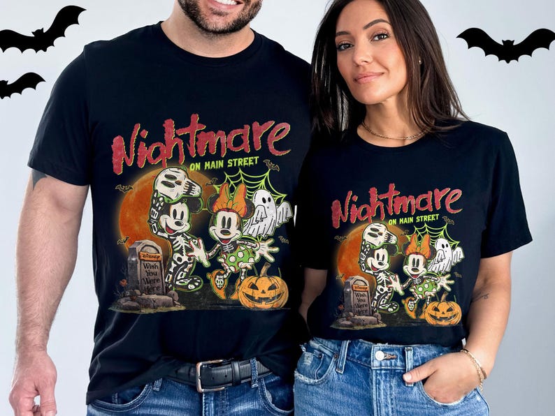 May include: Black t-shirts with a Halloween-themed graphic. The design features Mickey and Minnie Mouse as skeletons, a ghost, and a jack-o'-lantern, with the words "Nightmare on Main Street". Bats are in the background.