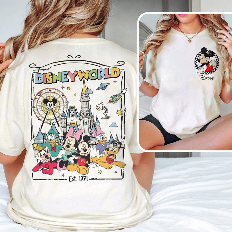 Op de afbeelding: Cr&egrave;mekleurig T-shirt met een Disney World-afbeelding op de achterkant met Mickey Mouse, Donald Duck, Minnie Mouse, Daisy Duck, Goofy en Pluto. De voorkant heeft een kleine Mickey Mouse-afbeelding met het woord "Daddy".