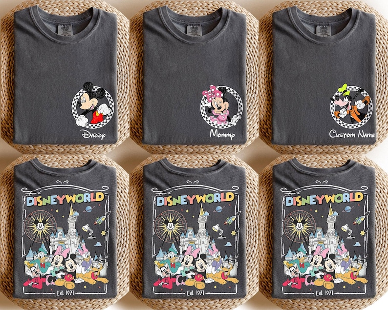 Op de afbeelding: Zes antracietgrijze t-shirts met Disney-ontwerpen. Drie shirts hebben Mickey, Minnie en Goofy in cirkelvormige frames met tekst. De andere drie shirts tonen een kleurrijke Disney World-afbeelding met personages en tekst.