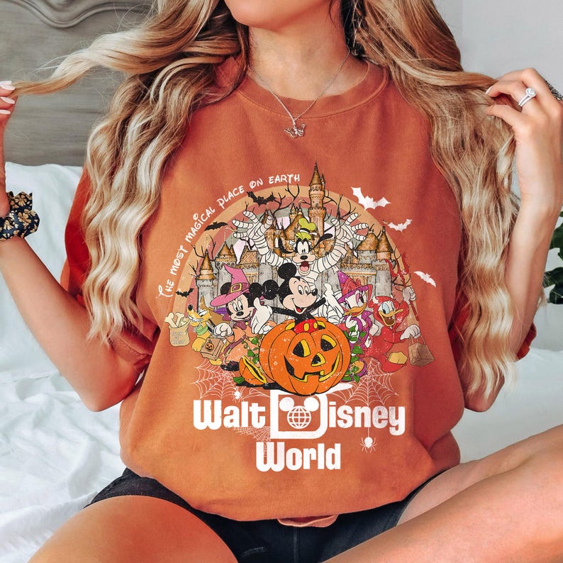 May include: Orange t-shirt with a graphic of Mickey Mouse and friends dressed in Halloween costumes in front of a castle. The text "The Most Magical Place on Earth" and "Walt Disney World" are printed on the shirt.