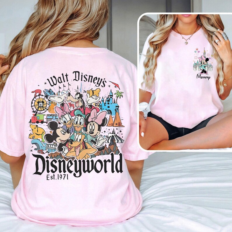 May include: Light pink t-shirt featuring a colorful Disney World graphic on the back with Mickey Mouse, Donald Duck, and other characters. The front of the shirt has a smaller graphic with Minnie Mouse and the word "Mommy".