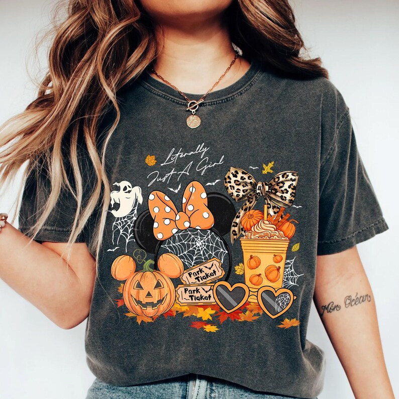 May include: Dark gray t-shirt with a Halloween-themed graphic. The design includes a Minnie Mouse head with an orange polka dot bow, a pumpkin, and the text "Literally Just A Girl".