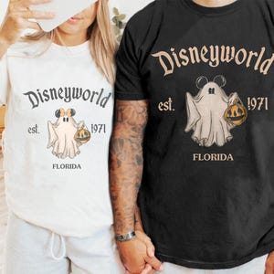 May include: White and black t-shirts with a Disneyworld graphic. The graphic features a ghost wearing Mickey Mouse ears and holding a pumpkin. The text "Disneyworld est. 1971 FLORIDA" is printed above and below the ghost illustration.
