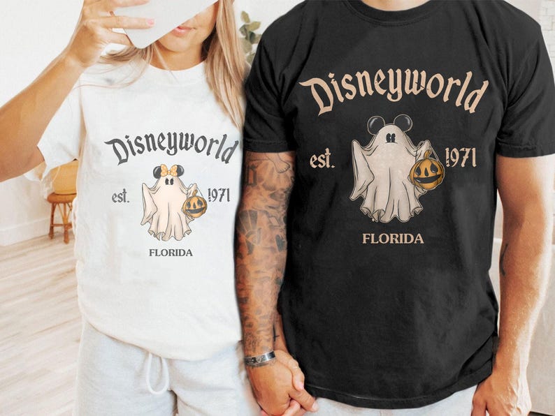 May include: White and black t-shirts with a Disneyworld graphic. The graphic features a ghost wearing Mickey Mouse ears and holding a pumpkin. The text "Disneyworld est. 1971 FLORIDA" is printed above and below the ghost illustration.