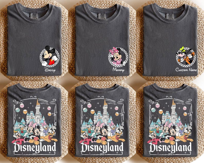 May include: Six charcoal gray t-shirts with Disney character designs. Some shirts feature Mickey and Minnie Mouse, and others display a Disneyland graphic with the text "Disneyland 1955". The shirts are folded on woven mats.