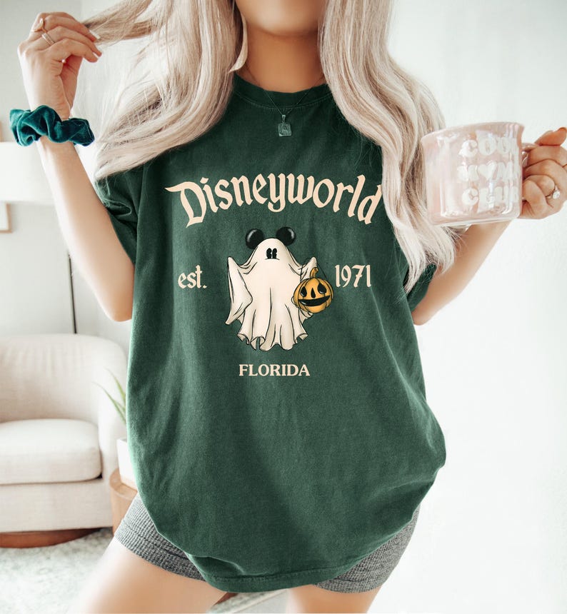Op de afbeelding: Groen T-shirt met een witte geest die een pompoen vasthoudt en de tekst "Disneyworld est. 1971 Florida".