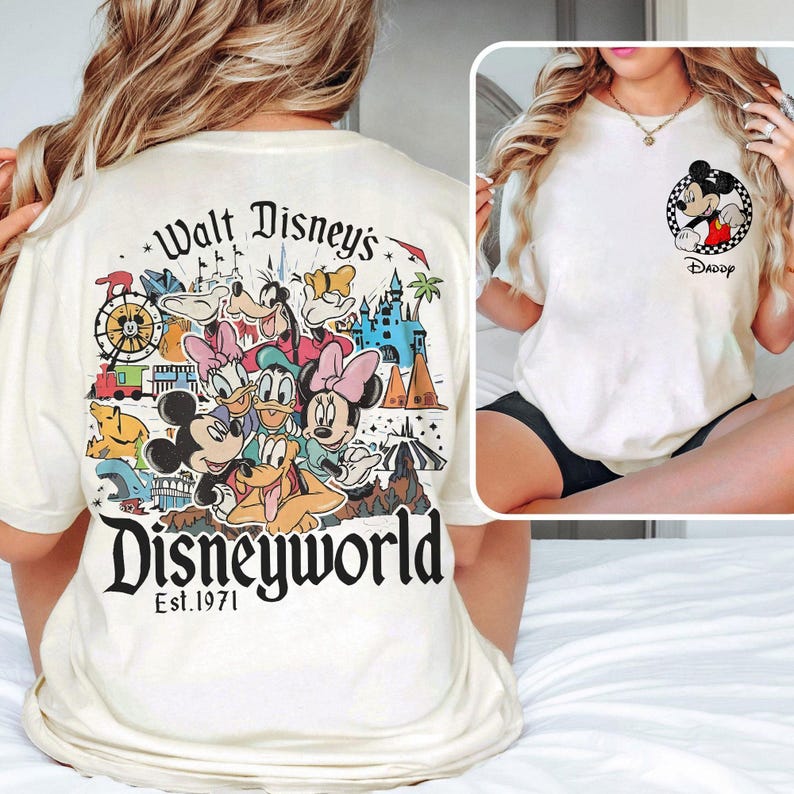 May include: Cream-colored t-shirt featuring a colorful Disney World graphic on the back with Mickey Mouse, Donald Duck, and other characters. The front of the shirt has a small Mickey Mouse graphic with the word "Daddy".